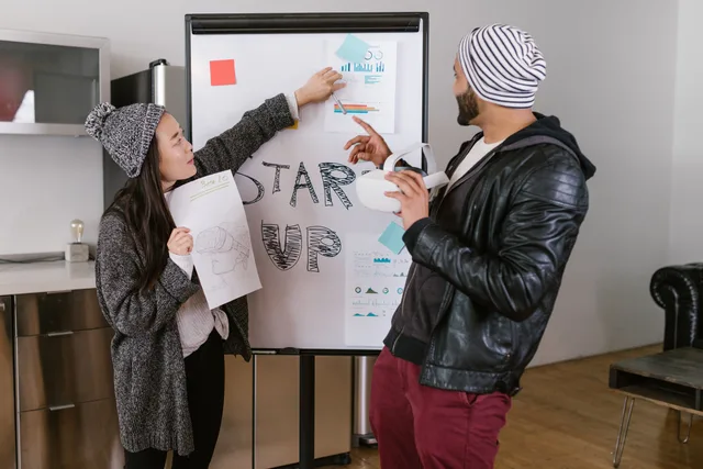 Two young adults presenting startup business ideas on a flipchart indoors. Startup funding rules and ethics: an England checklist